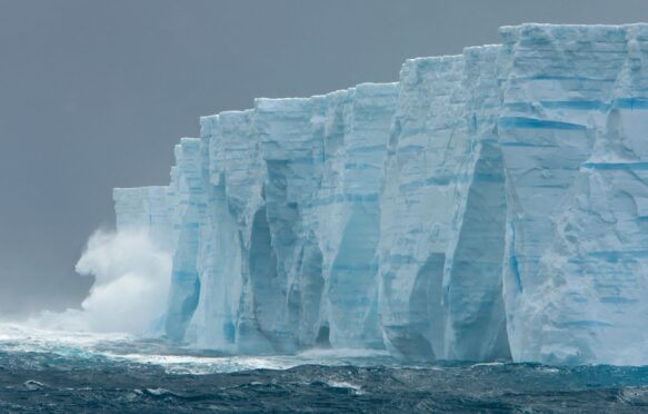 Waves crashing against ice cliffs of iceberg in Southern Ocean.